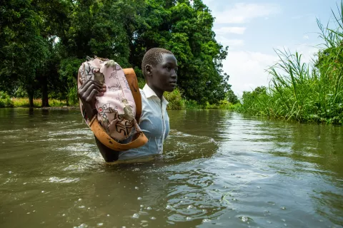 A young girl holding up her excisise book to keep it out of the flood water