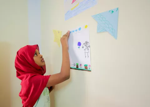 A girl puts up a drawing on a wall