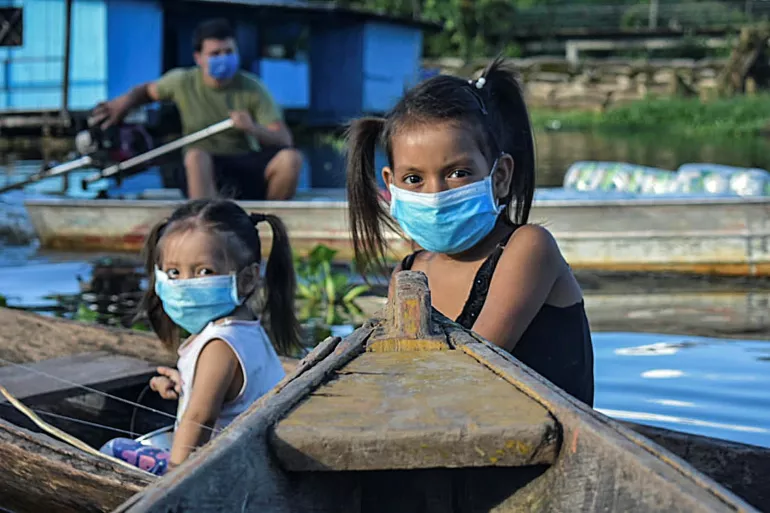 Two girls wearing face masks as a preventive measure against the spread of COVID-19 sit in a boat in the Amazon river in Leticia, Colombia.
