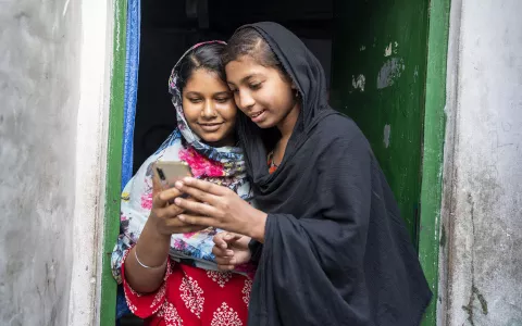 A girl, 14, is showing her friend something in her mobile phone