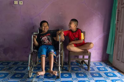 A child with a physical impairment, sits next to his best friend, a child with a visual impairment