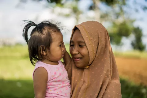 Jamila holds her 13-month-old daughter Jonaila while walking around a small crop field. Tomorrow Jonaila will receive her first vaccines.