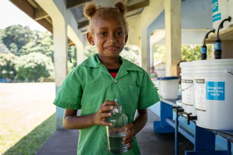 Student of Qatuneala Primary school in Vanuatu with container of clean water to drink at school from WASH infrastructure.