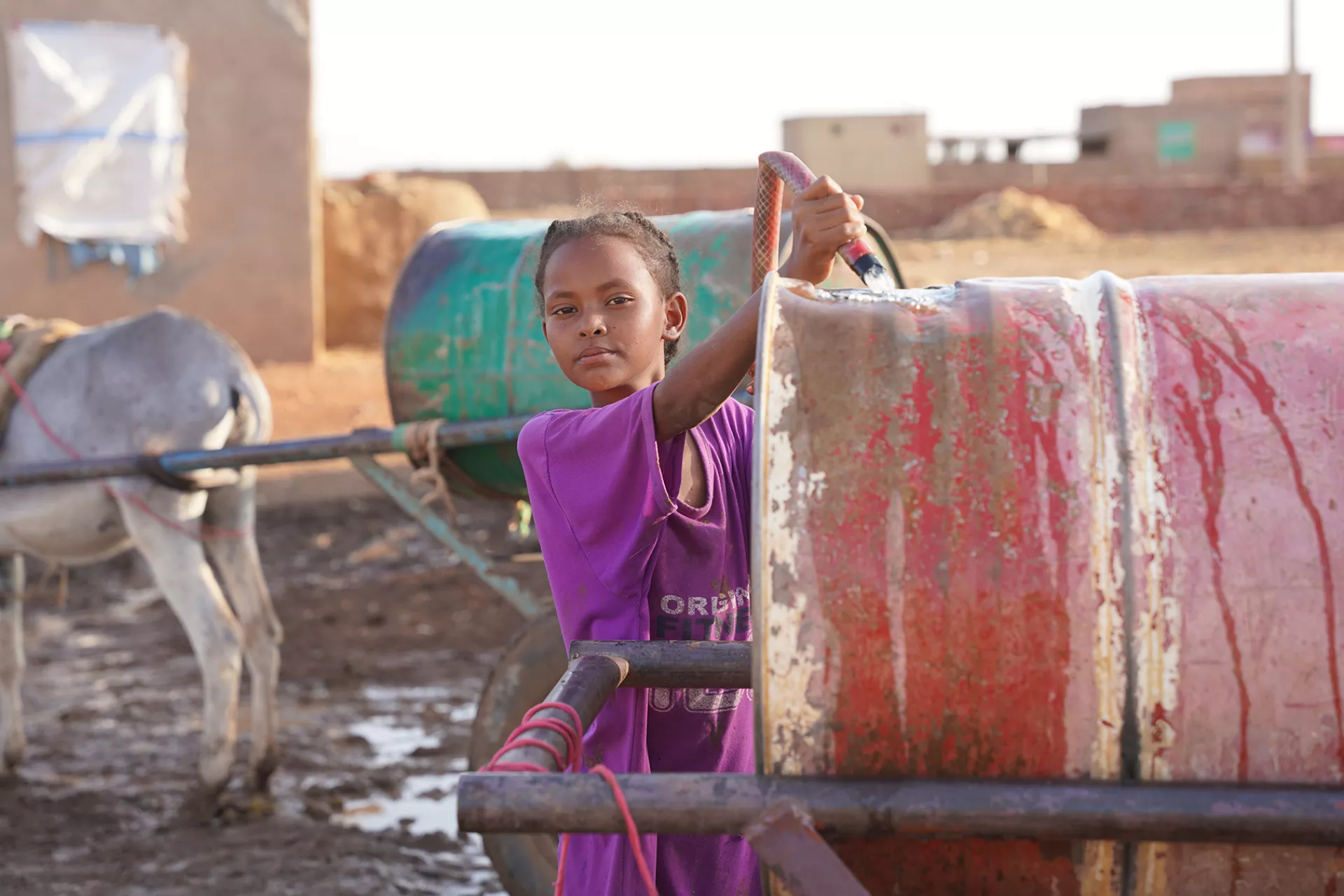 A 9-year-old girl in Sudan fills a drum with water at a well that she frequents