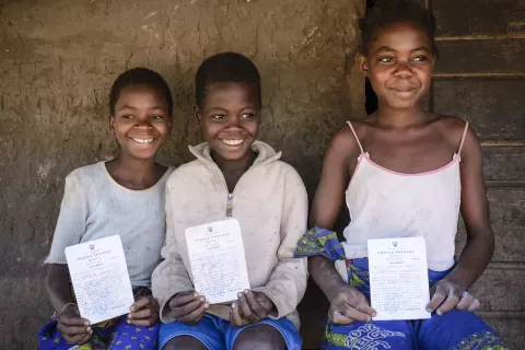 Three children in Mozambique showing their birth certificates