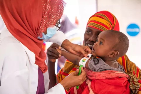 A health worker measures the arm of a child to assess his nutrition status