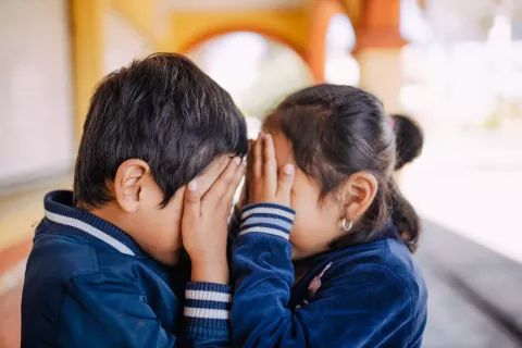 Two children facing each other and covering their eyes