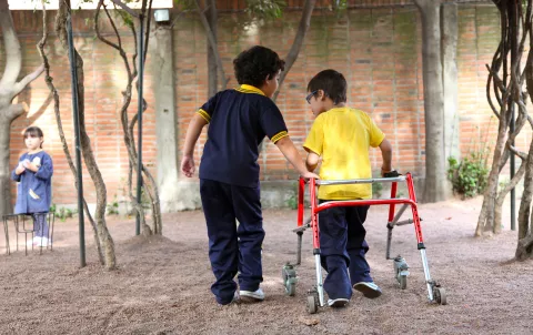 Two boys, one who is using a walker, walk side by side outdoors during a break between classes. Uruguay