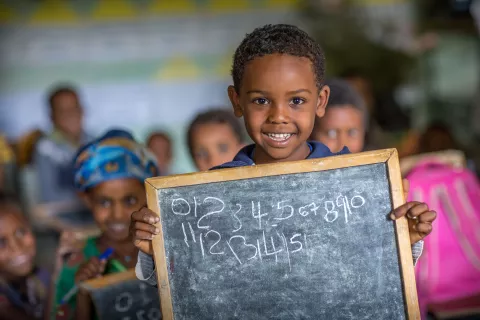 A boy, 6, smiles holding his little black board after writing numbers on it. 