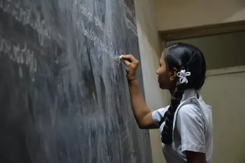 Young teen writing with chalk on a blackboard in school