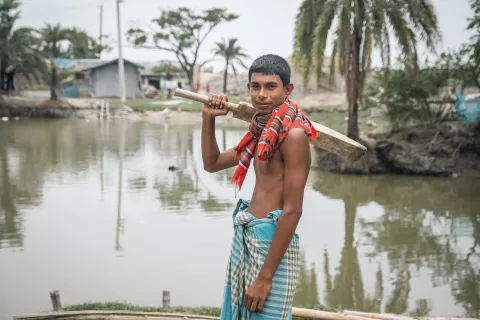 A boy sports a cricket bat over his shoulder amid a backdrop of flooded plains 