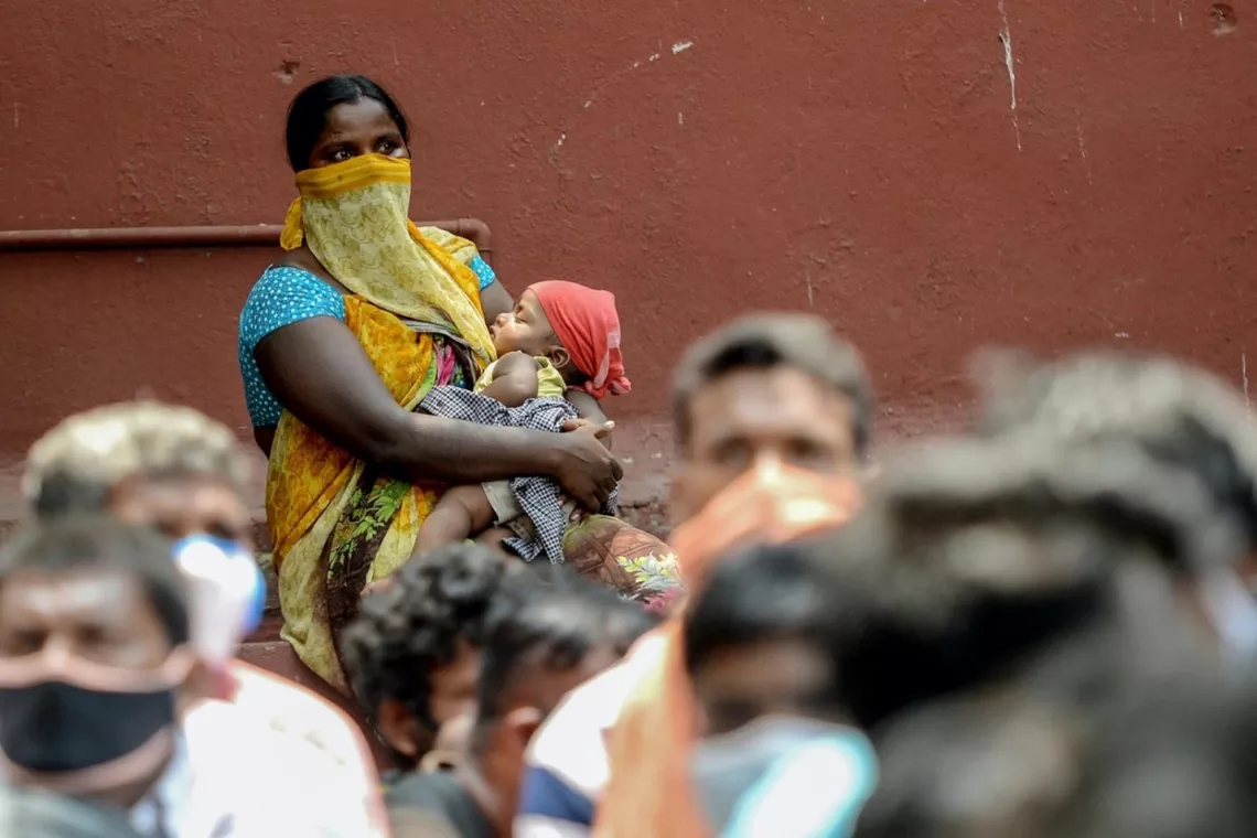 Chennai, India: a woman carries a child alongside other migrant workers waiting to board a special train to Bihar state after the government eased a nationwide lockdown to help prevent the spread of COVID-19.