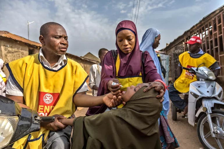 On a street in Nigeria, two health workers provide an oral polio vaccine to a child.
