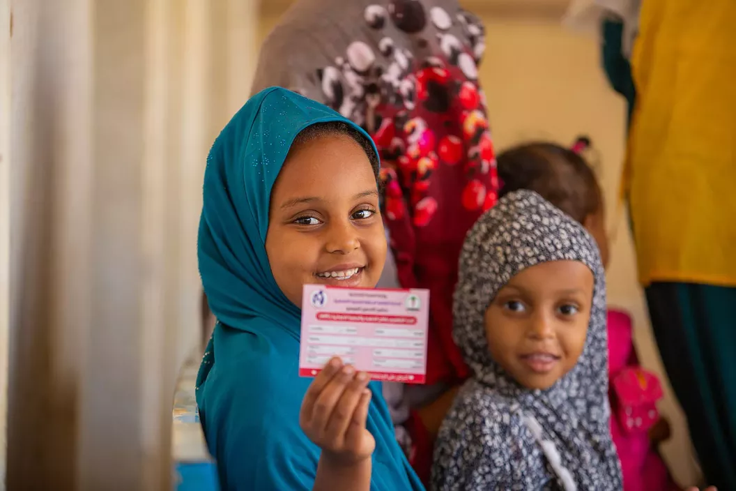 A girl, with a younger girl beside her, shows her vaccination card.